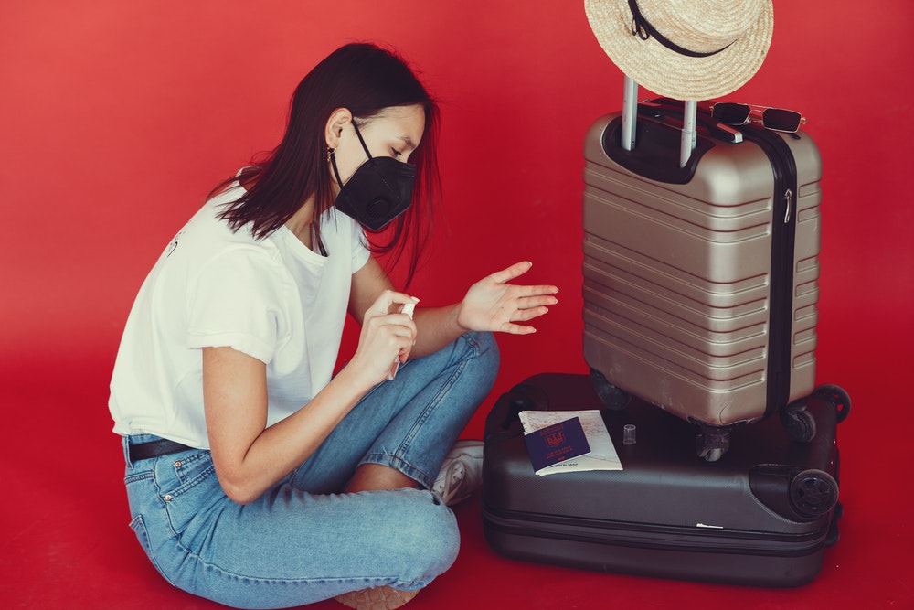 Young woman with suitcase using hand sanitizer
